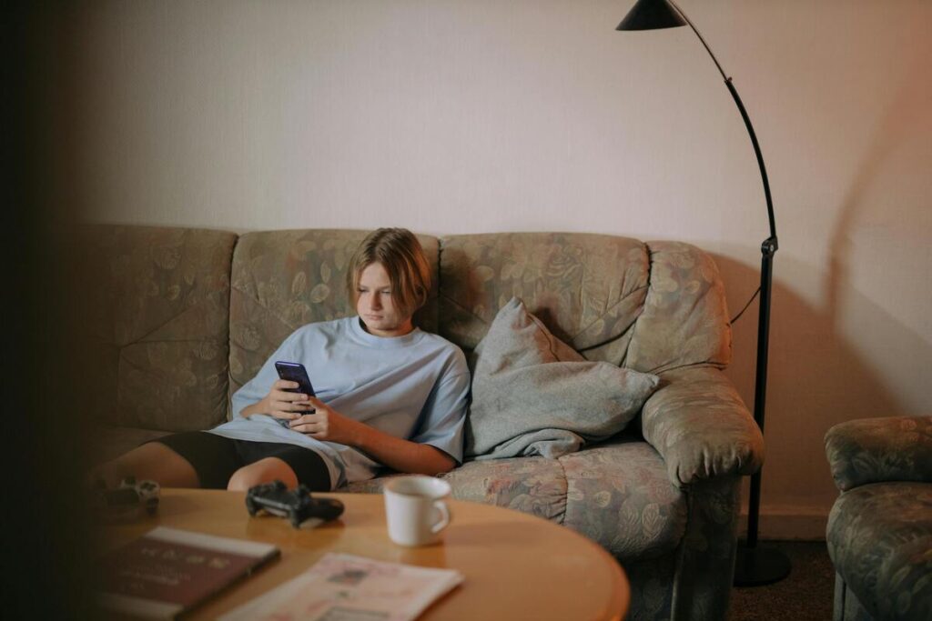 Tinejdžerica sjedi na kauču i gleda u mobitel