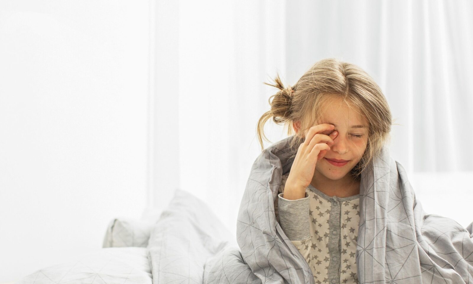 Djevojčica pokrivena sjedi na krevetu