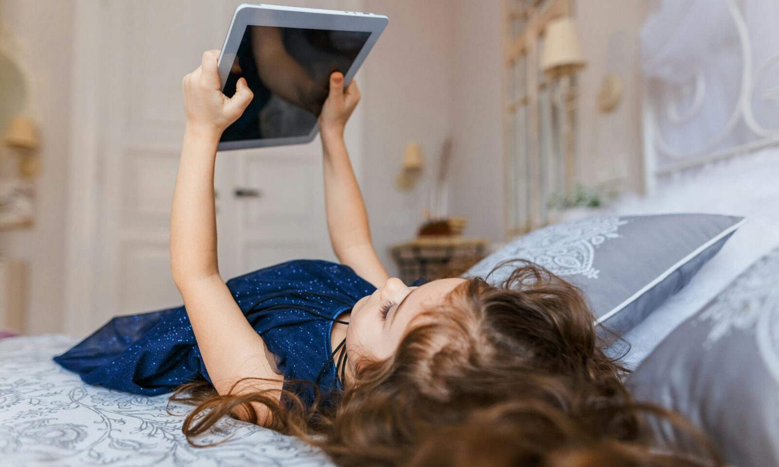 Djevojčica leži na krevetu gleda sadržaj na tabletu
