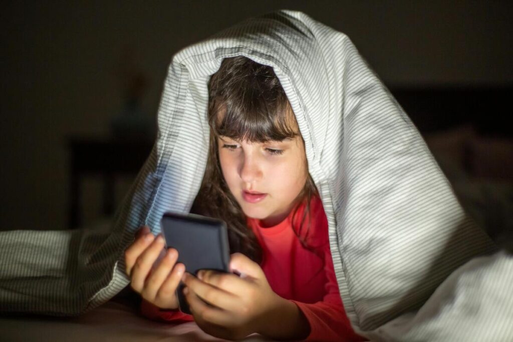 Dijete potajice u krevetu gleda sadržaj na mobitelu