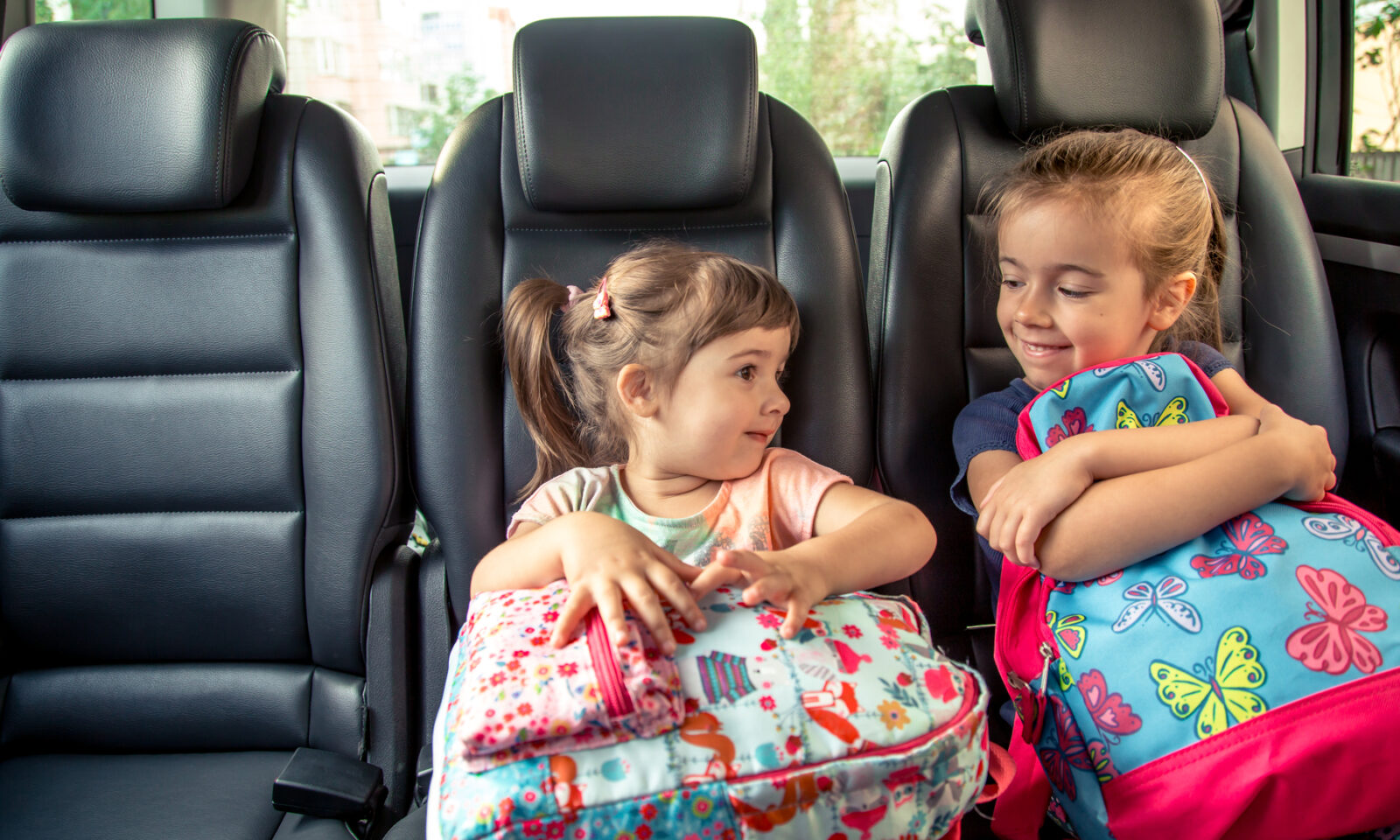 Djevojčice s ruksacima na stražnjem sjedalu automobila