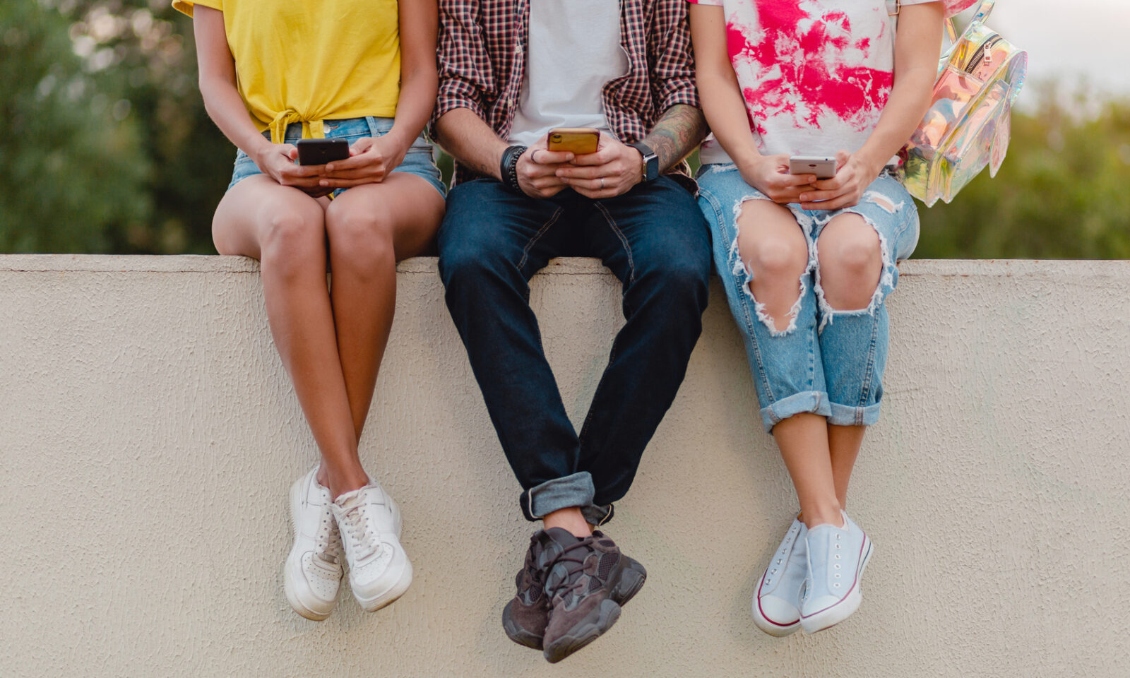 Tinejdžeri sjede na zidiću i gledaju sadržaj na mobitelu